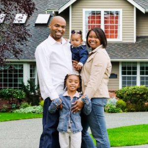 Portrait of a young family standing on the porch in front of their home.