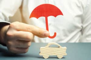 An insurance agent is holding a red umbrella over a miniature wooden car. Auto insurance concept. Vehicle protection. Insurance company services. Gesture of protection. Safety and security
