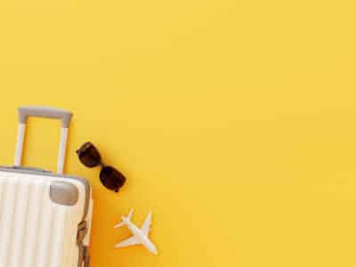 white suitcase, a pair of sunglasses and a toy airplane against a yellow background