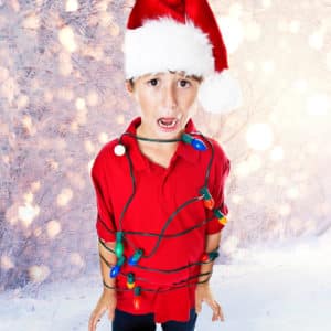 Young boy wearing Santa hat wrapped in string of lights