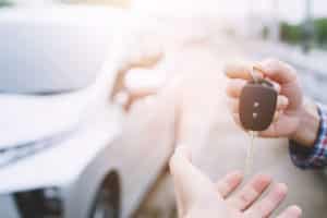 Businessman handing over gives the car key to the other woman on car background.