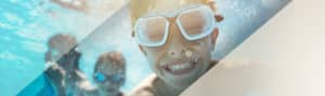 Child swimming beneath water smiling while wearing goggles