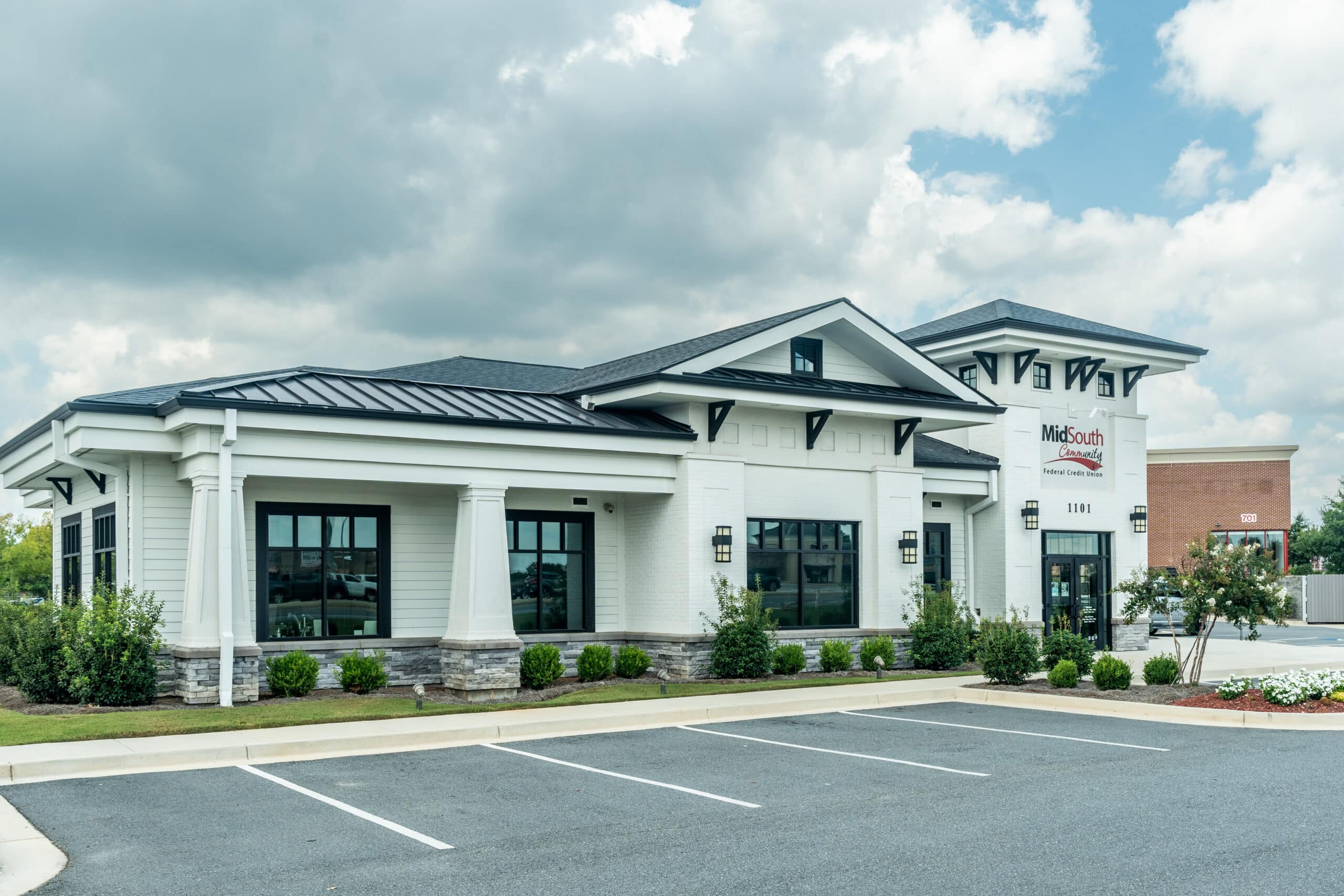 A modern, single-story commercial building with white walls and black trim beside a mostly empty lot under clouds. Sign reads MidSouth Community Federal Credit Union.