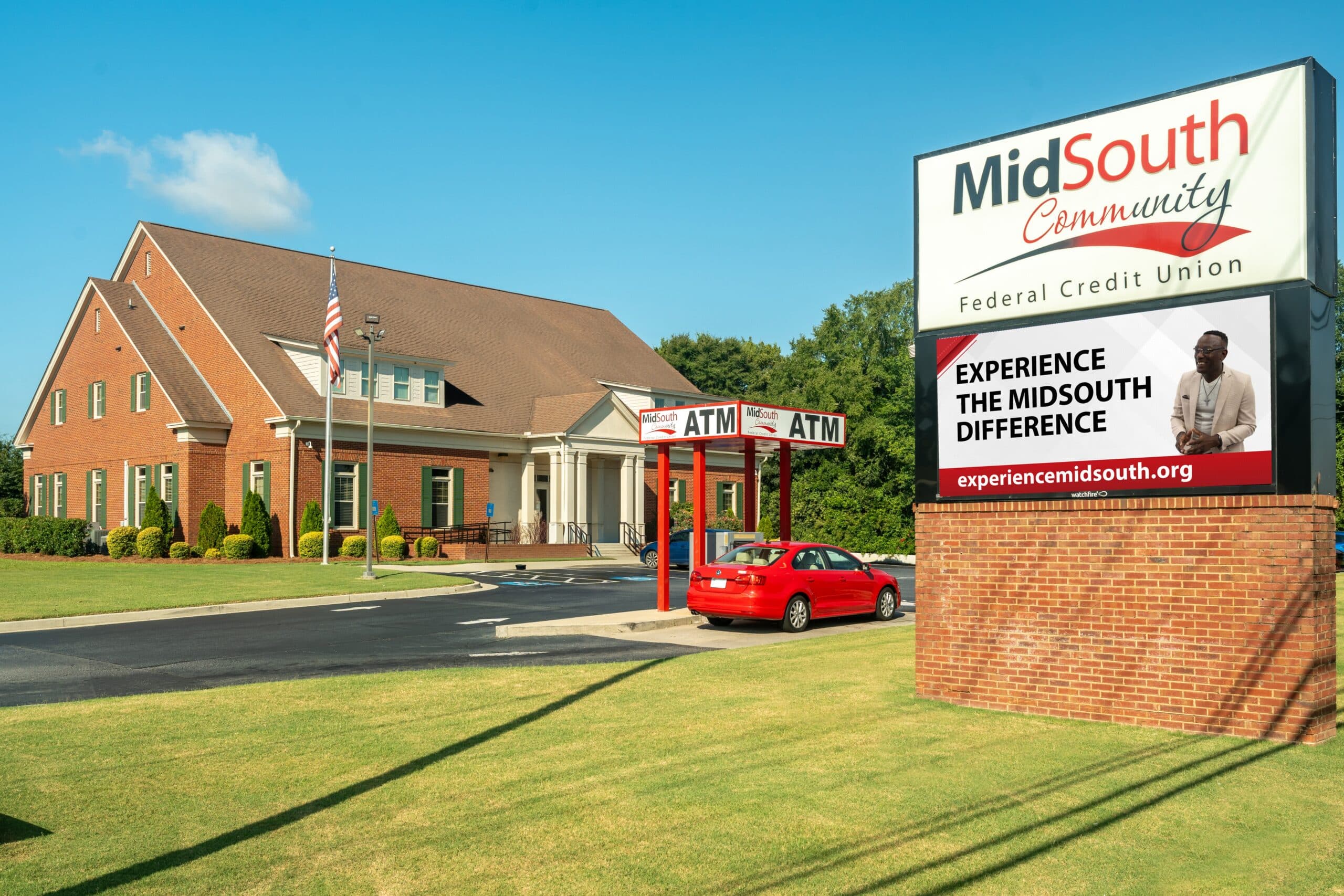 A red brick building with a drive-thru ATM, a red car outside, and a large sign for MidSouth Community Federal Credit Union.