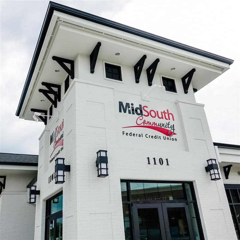 A white brick building with black accents houses the MidSouth Community Federal Credit Union. The address 1101 is above the entrance, under a cloudy sky.