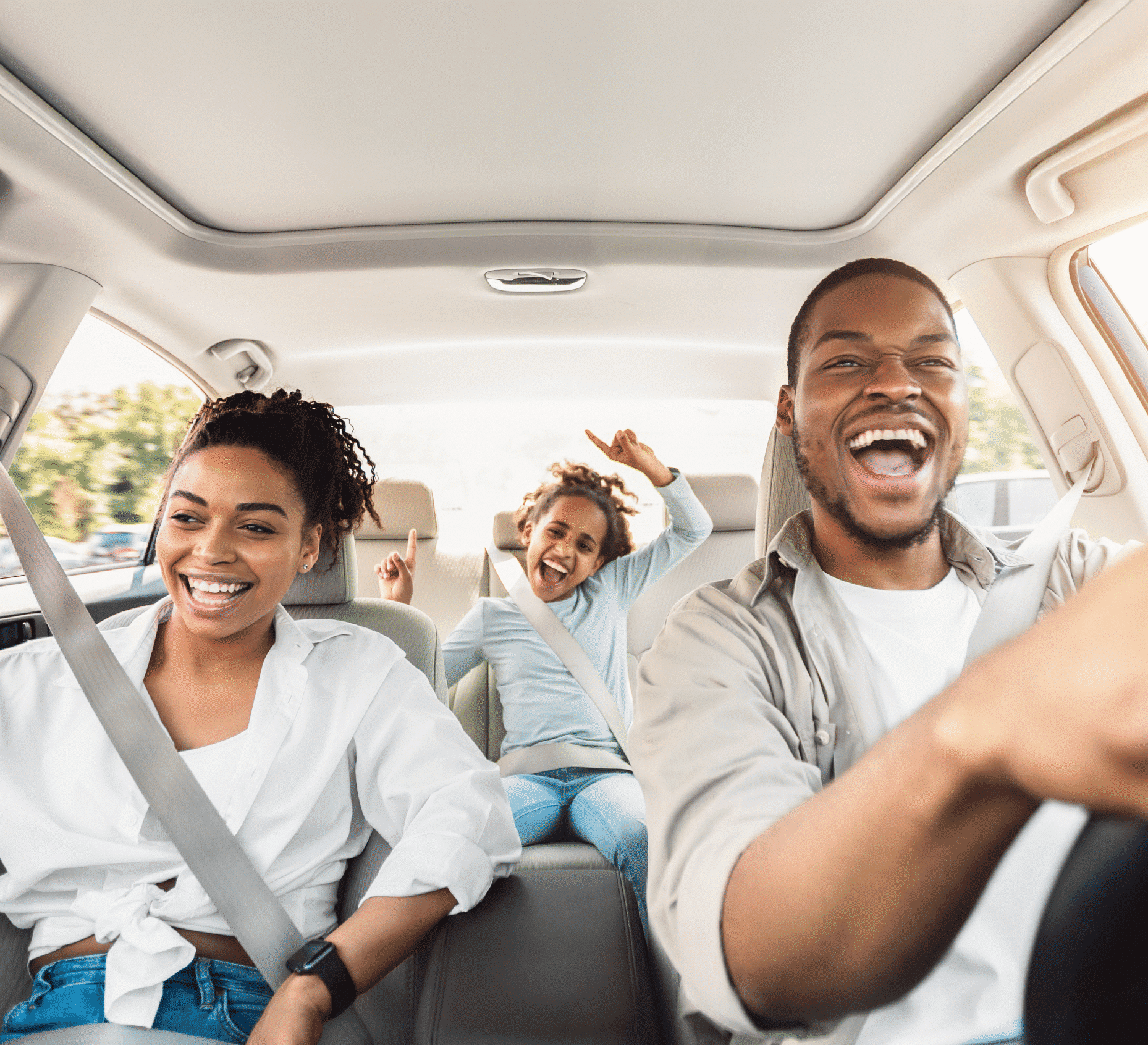 A cheerful family of three enjoys a sunny car ride; dad drives smiling, mom laughs in front, and their daughter raises her arms joyfully.