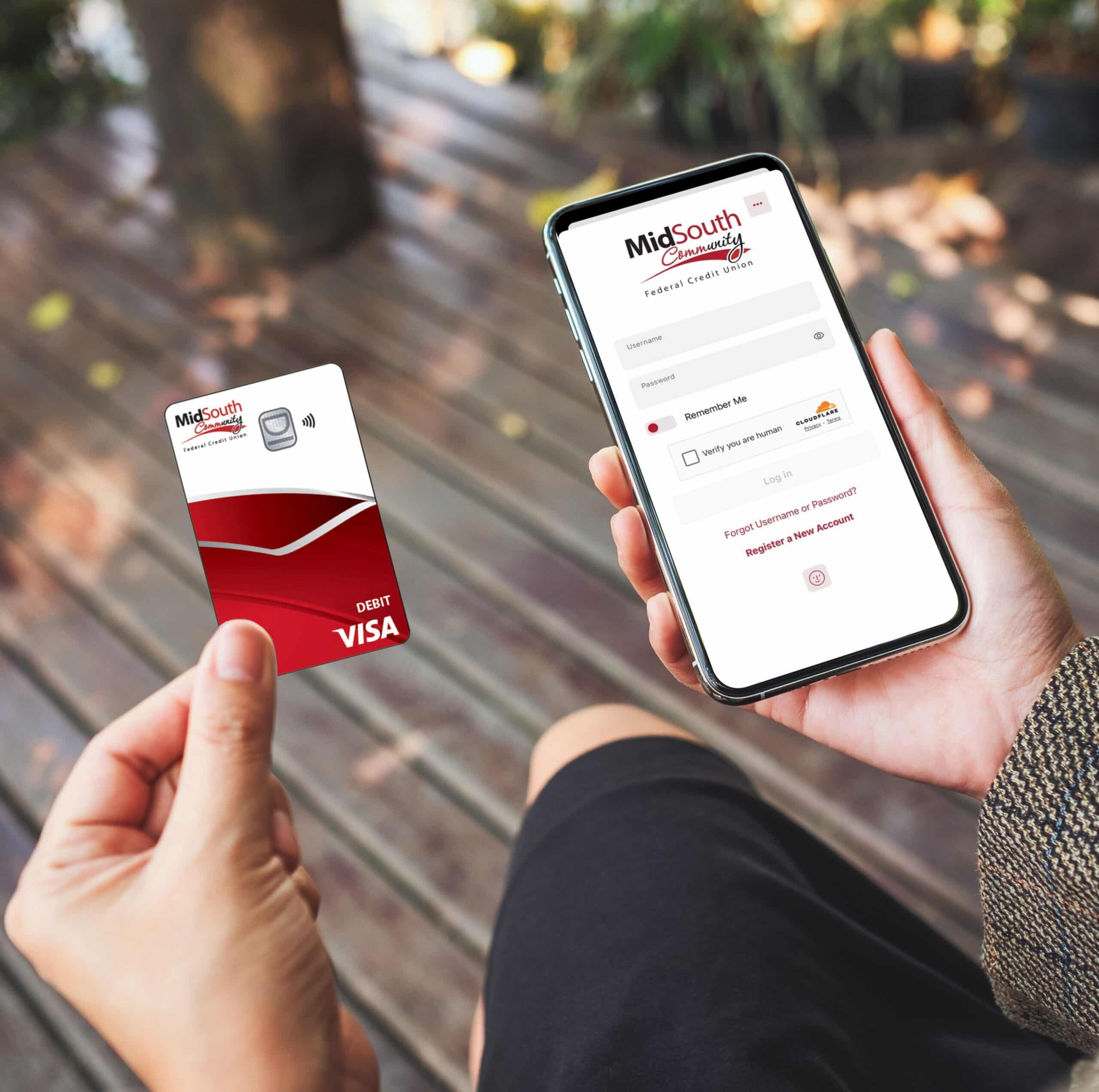 A person holds a MidSouth Community debit Visa card in one hand and a smartphone with the credit union mobile banking login screen.