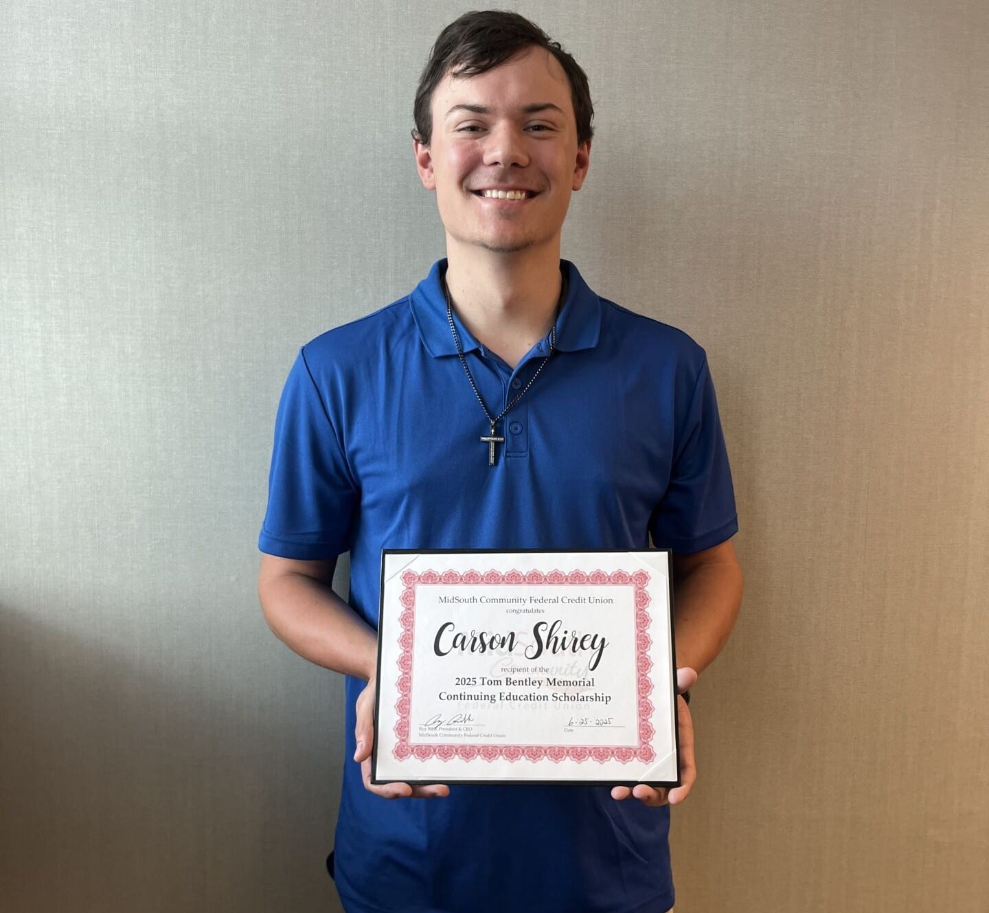 A young man in a blue shirt smiles while holding a certificate for the 2023 Toni Bently Memorial Continuing Education Scholarship.