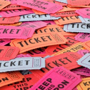 A large pile of colorful raffle tickets and coupons in red, orange, pink, and gray with the words TICKET and KEEP THIS COUPON in bold black letters.