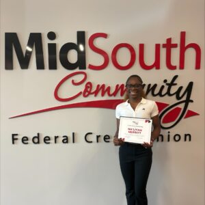 A person stands smiling, holding a certificate in front of a wall with the words MidSouth Community Federal Credit Union.